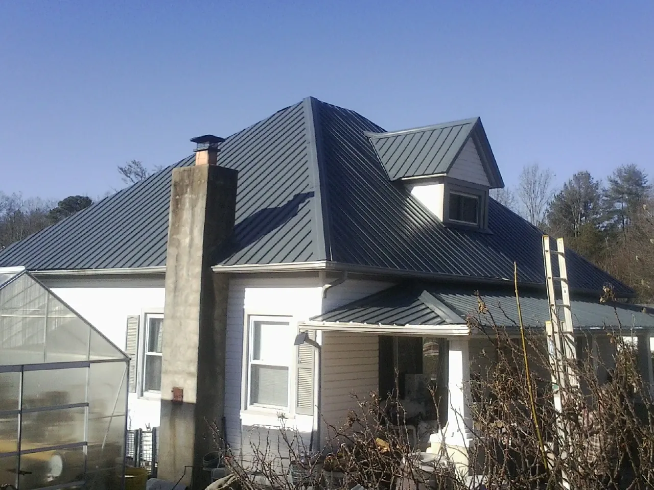 Dark blue standing seam metal roof on a white farmhouse with dormer — Slate & Tile Roof Repair by Roofing Brothers in Bear