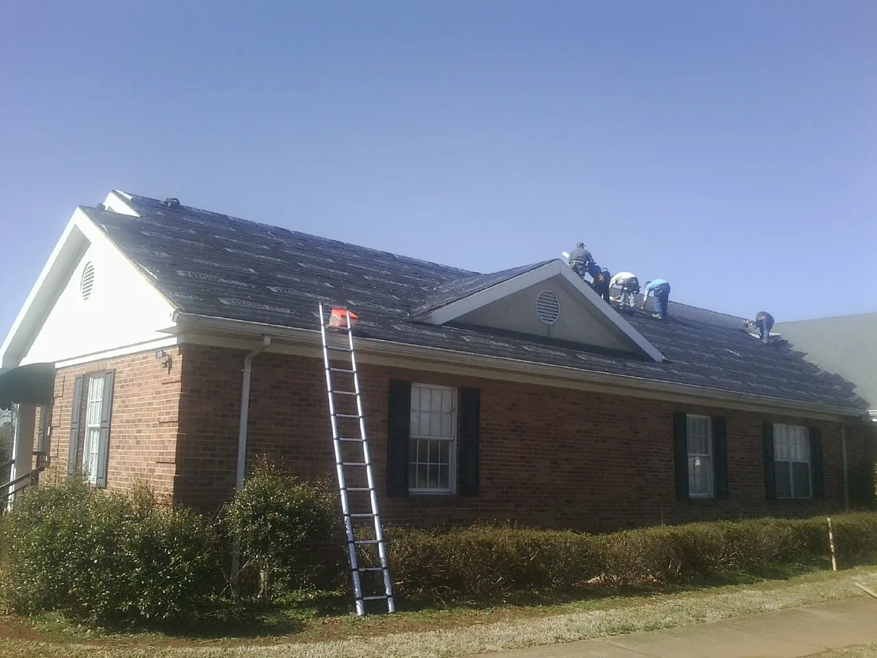 Crew tearing shingles off a brick ranch roof with a ladder set — Emergency Roof Repair work by our crew in Bear