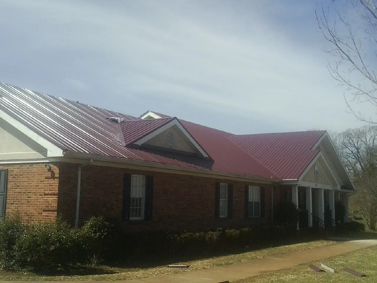 Red metal roof with gabled entries on a long brick building, from a Hail Damage Roof Repair job in Bear